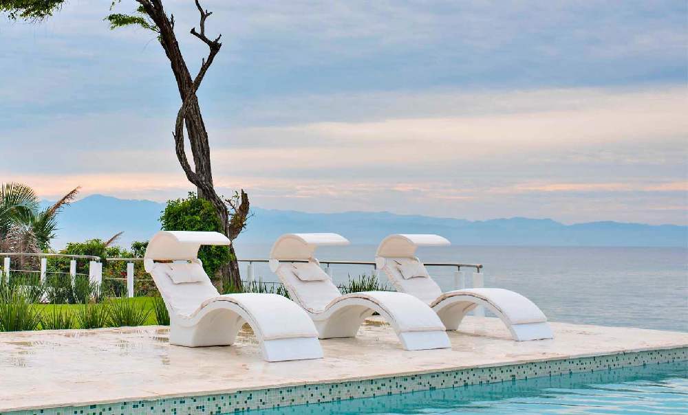 Luxury white chaise lounges with built-in canopies overlooking an infinity pool and ocean view for upscale commercial resort pool decks.